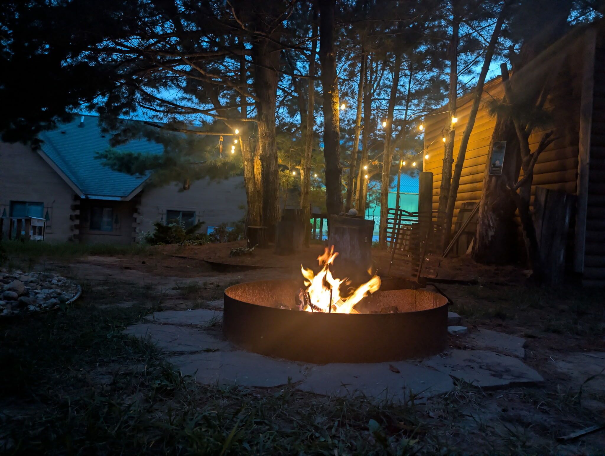 A fire pit in a wooded area with a house in the background.