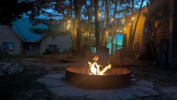 A fire pit in a wooded area with a house in the background.
