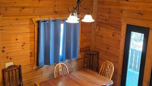 A wooden interior with a dining table, chairs, and a hanging light fixture.