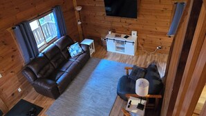 A wooden cabin interior with a sofa, a chair, a TV mounted on the wall, and a small table.