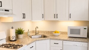 A modern kitchen with white cabinets, a gas stove, a microwave, and a dishwasher.