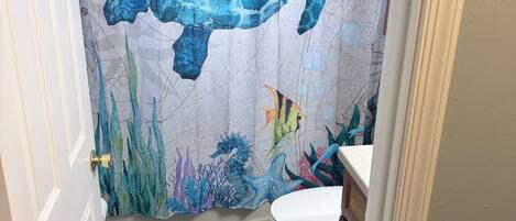 A bathroom with a seahorse and turtle shower curtain, a wooden floor, and a white toilet.