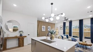 Una cocina moderna con una isla central, un comedor con sofá y mesa, y ventanas amplias con cortinas.