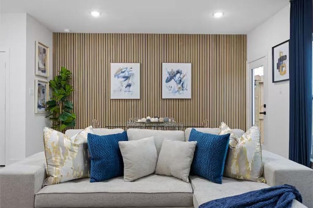 A modern living room with a sofa set, framed artwork on the wall, and a vertical wooden panel.