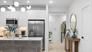 Una cocina moderna con armarios blancos, electrodomésticos de acero inoxidable y una isla central con taburetes de bar.