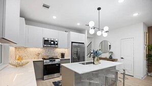 Una cocina moderna con armarios blancos, electrodomésticos de acero inoxidable y una isla central con taburetes.