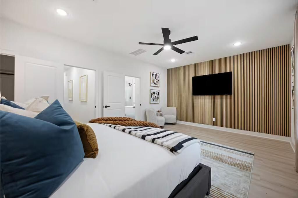 Ein modernes Schlafzimmer mit Bett, Deckenventilator, montiertem Fernseher und einer Wandpaneele aus Holz.