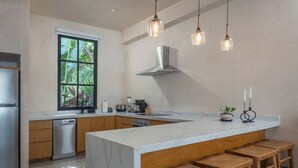 Una cocina moderna con una isla grande, taburetes de madera, un refrigerador de acero inoxidable e iluminación colgante.