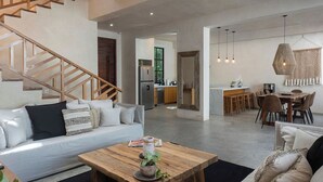 Una sala de estar moderna con una escalera de madera, una cocina al fondo y un comedor con una mesa y sillas de madera.