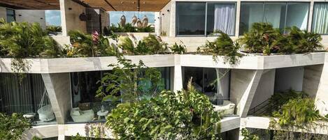 A modern multi-story building with a flat roof, large windows, and extensive greenery.