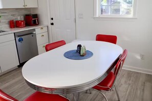 Een eetgedeelte met een witte tafel, rode stoelen en een keuken op de achtergrond.