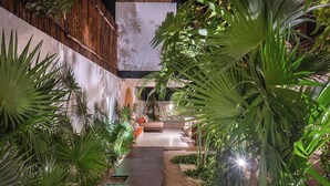 A wooden pathway leading to a seating area surrounded by lush green plants and a stone wall. - Villa Itze | 5Bdrm Jungle Oasis w/ Pool & BBQ<br>Dedicated concierge<br>Beach access (Tulum)