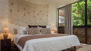 A bedroom with a large bed, two bedside tables with lamps, a macrame wall hanging, and a view of greenery through a sliding door. - Villa Itze | 5Bdrm Jungle Oasis w/ Pool & BBQ<br>Dedicated concierge<br>Beach access (Tulum)