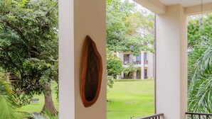 Un balcon doté de meubles en osier, d’un ventilateur de plafond et offrant une vue sur une pelouse verdoyante et des bâtiments en arrière-plan.