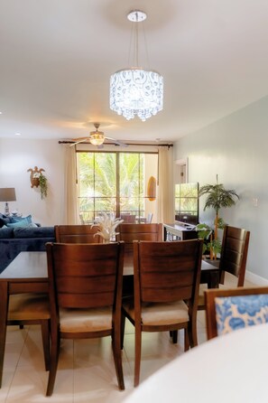 A dining area with a table and chairs, a ceiling fan, and a window with curtains. - Beautiful central 3-bedroom Condo with Pool and Beach Club Access (Coco)