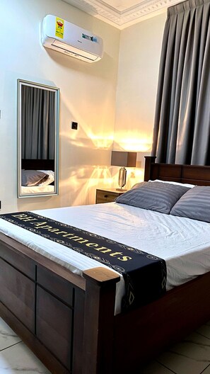 Una habitación de hotel con cama, mesita de noche, lámpara, espejo y aire acondicionado.