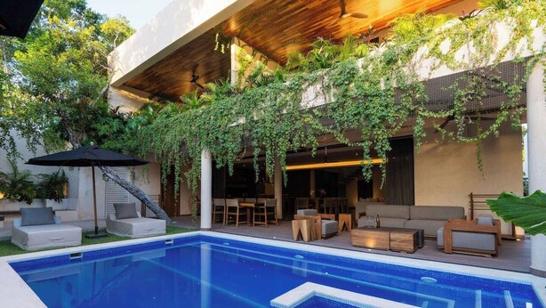 Een modern buitenzwembad met houten overkapping, loungezitmogelijkheden en een overdekt zitgedeelte met planten.
