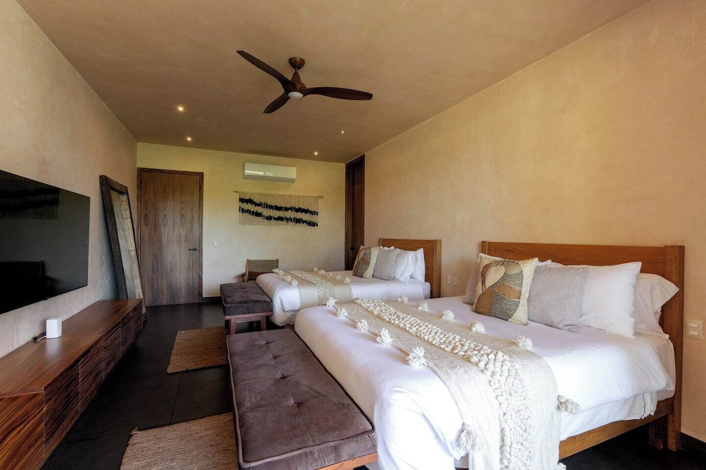 Ein Hotelzimmer mit einem großen Bett, einem kleineren Bett, einem Fernseher und einem Deckenventilator.
