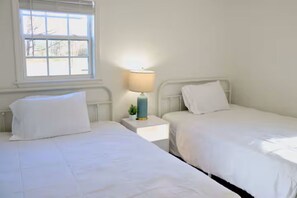 Ein Zimmer mit zwei Einzelbetten, einem kleinen Nachttisch mit Lampe und einem Fenster mit Jalousien.