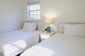 Ein Zimmer mit zwei Einzelbetten, einem Nachttisch mit Lampe und einem Fenster mit Jalousien.