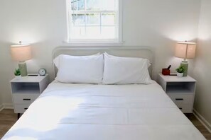 Ein Schlafzimmer mit einem großen Bett, zwei Nachttischen mit Lampen, einem Fenster und einer kleinen Uhr auf einem Tisch.