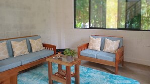 Une pièce avec un canapé bleu, une petite table en bois et une grande fenêtre donnant sur un paysage verdoyant.