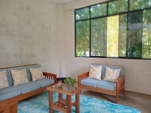 A room with a blue sofa, a wooden coffee table, and a large window with a view of trees.