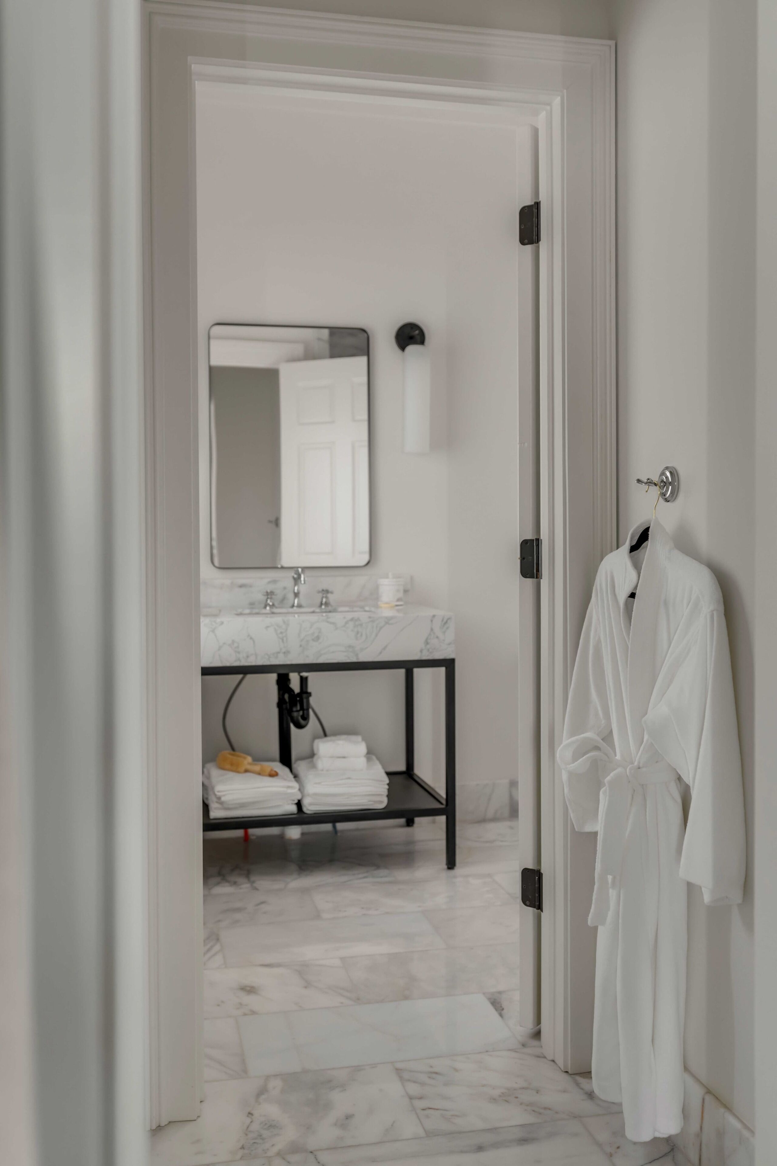 A bathroom with a white sink, a mirror, a towel rack, and a marble floor.