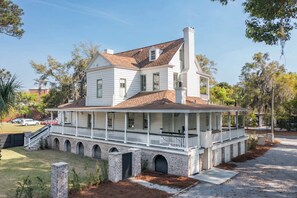 Une maison blanche à deux étages, dotée d’un porche, de fondations en briques et d’une cheminée.