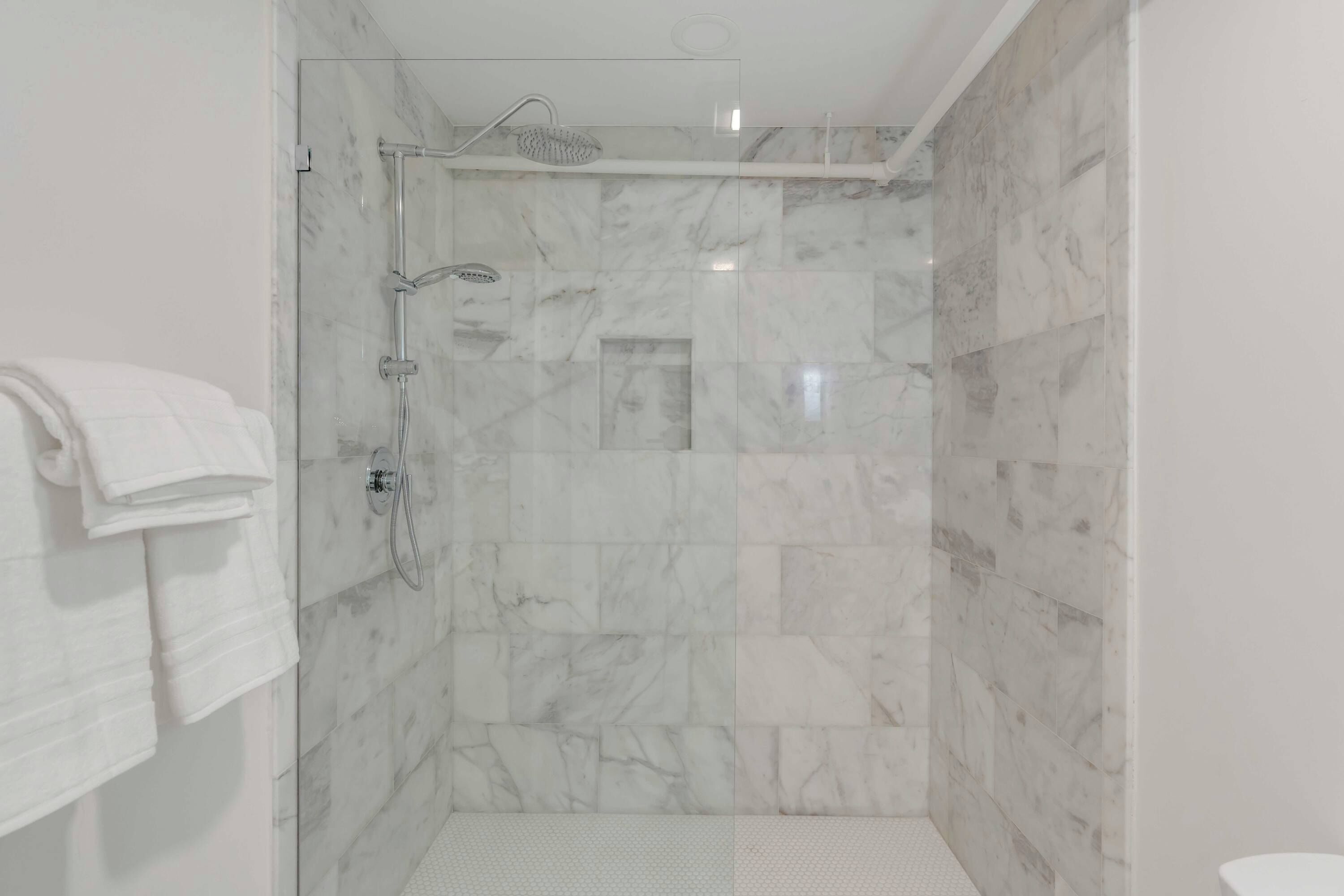 Une douche fermée par des parois en verre, dotée d’un pommeau de douche à main et d’un robinet mural.
