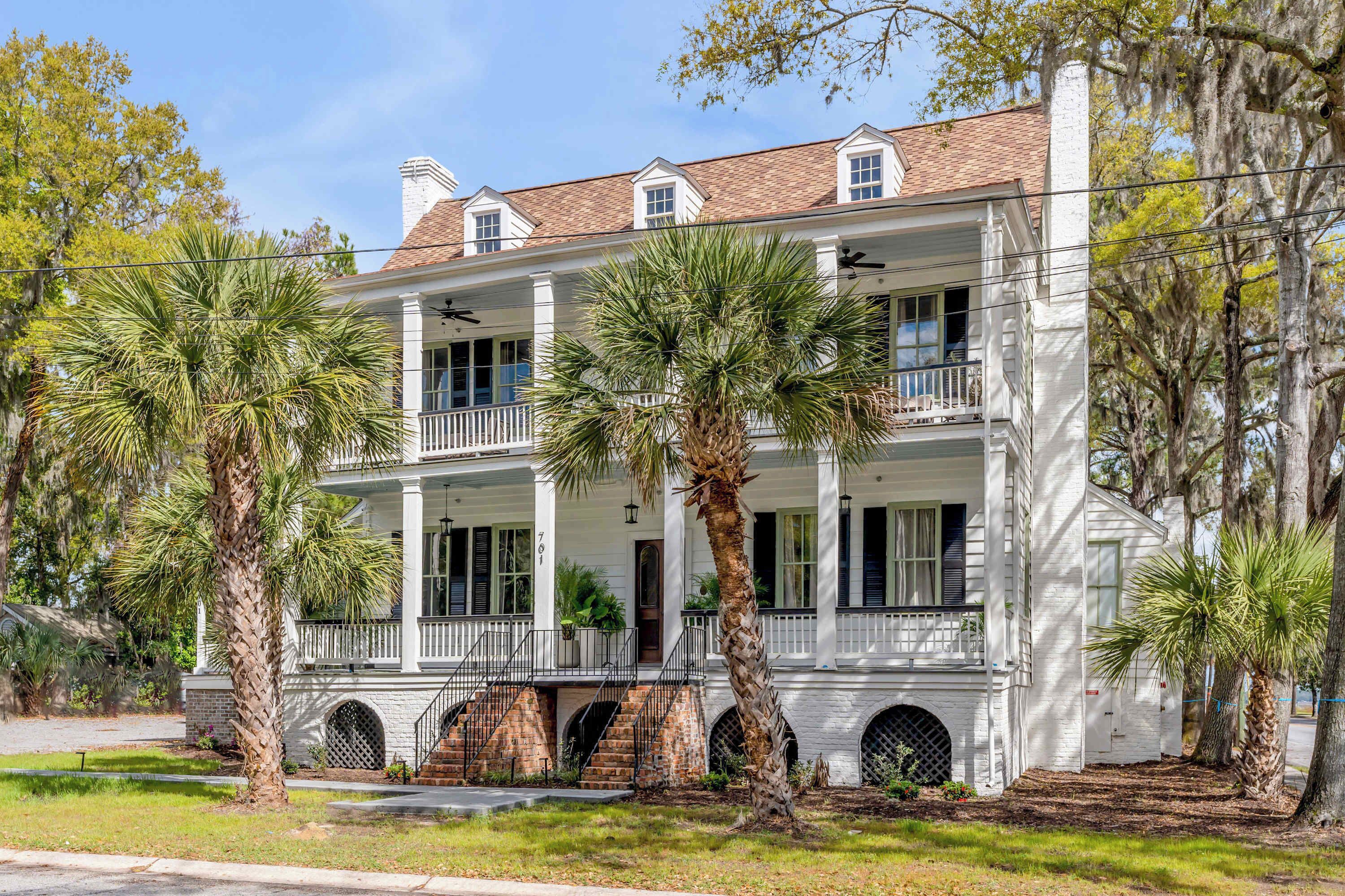 A two-story white building with a balcony, palm trees, and a brick base.