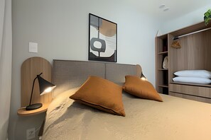 Une chambre à coucher comprenant un lit, deux lampes de chevet, une tête de lit, une œuvre d’art abstraite accrochée au mur, une armoire en bois et une plante.