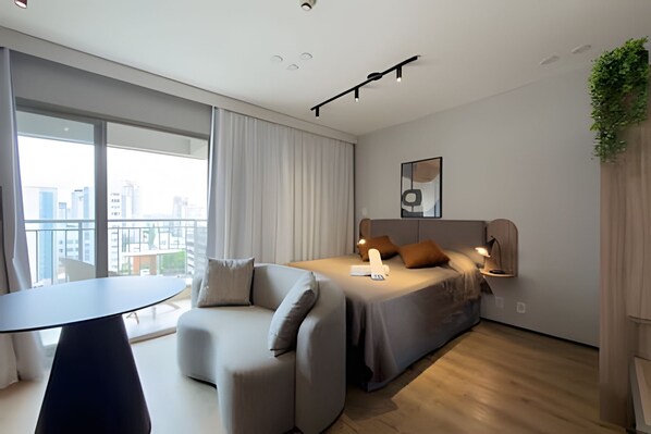 A modern bedroom with a bed, a sofa, a small table, and a view of the city. - Ape em Perdizes 8 andar prox. ao Allianz (São Paulo)
