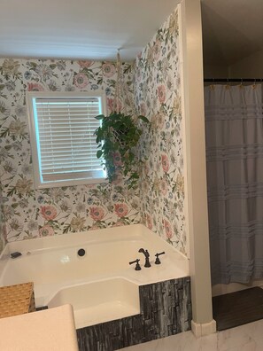 Um banheiro com papel de parede floral, uma banheira, uma janela com persianas e um cortina de chuveiro.