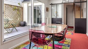 A modern room with a glass table, chairs, a view through large windows, and a colorful rug. - ArchiDuck, votre appartement maison terrasse parking (Rouen)