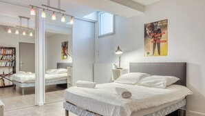 A modern bedroom with a large bed, bedside tables, a mirror, a bookshelf, and a poster on the wall. - ArchiDuck, votre appartement maison terrasse parking (Rouen)