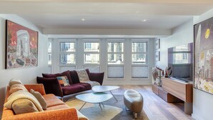 A modern living room with a sofa, coffee table, ottoman, and a flat-screen TV. - ArchiDuck, votre appartement maison terrasse parking (Rouen)