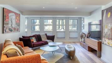 A modern living room with a sofa, coffee table, ottoman, and a flat-screen TV.
