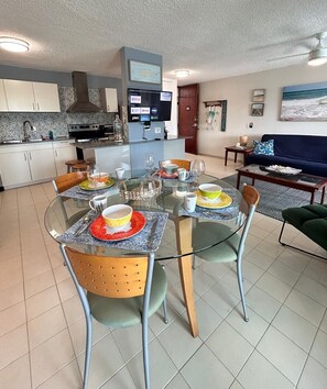 Een moderne keuken met een flatscreen televisie, een eettafel met stoelen en een zithoek met een bank en een schilderij.