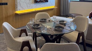 Zona pranzo moderna con tavolo in vetro, sedie e TV fissata a una parete in marmo.