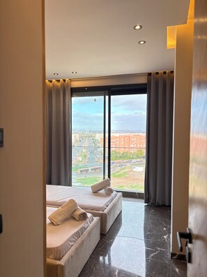 Une chambre d’hôtel avec deux lits, une grande fenêtre avec des rideaux, une vue sur la ville et un sol en marbre.
