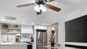 Un salon moderne dotĂ© dâun ventilateur de plafond, dâun tĂ©lĂ©viseur, dâun coin cuisine avec un rĂ©frigĂ©rateur et dâune table Ă manger avec des chaises.
