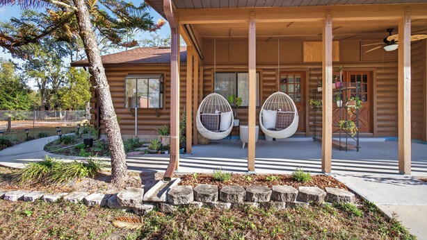 Une cabane en rondins avec un porche, deux fauteuils Ă bascule et un petit jardin.