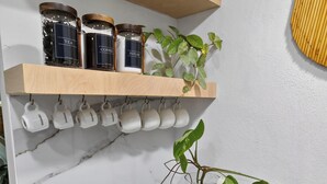 Un comptoir de cuisine avec une machine à café, une plante dans un vase et une étagÚre avec des bocaux et des tasses.