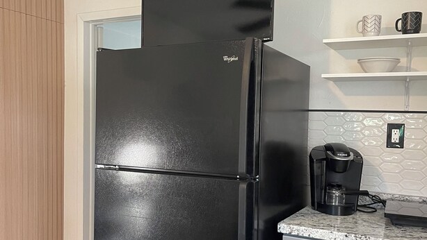 A black Whirlpool refrigerator with a built-in ice maker, a coffee maker on the countertop, and a white tiled backsplash. - Cozy apartment in Valrico (Valrico)