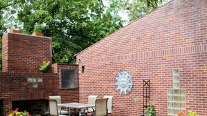 A brick patio with a table and chairs, a decorative sun wall art, and potted plants. - Guesthouse – 5BR Lower Level (2BR+3BR) (Overland Park)