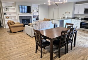 Un salon moderne avec une cheminée, une table à manger avec des chaises, un canapé et un téléviseur fixé au mur.