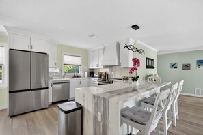 A modern kitchen with white cabinetry, a stainless steel refrigerator, and a marble island. - Modern 3BR Retreat Near Siesta Key + Private Yard (Sarasota)