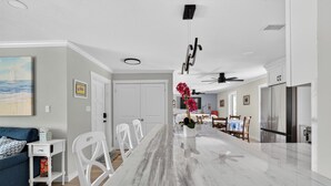 Uma cozinha moderna com bancada de mármore, armários brancos e um espaço de refeições com cadeiras.