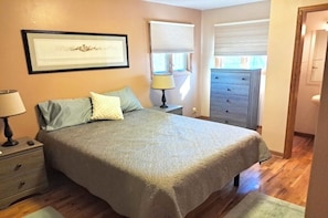 Une chambre à coucher comprenant un lit, une table de chevet, une lampe, une commode et une œuvre d’art encadrée accrochée au mur.